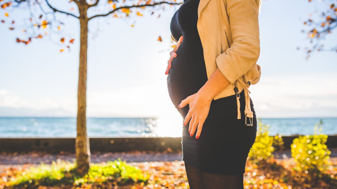 pregnant woman wearing beige long sleeve shirt standing near brown tree at daytime